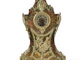 a gold and red clock on a stand on a white surface