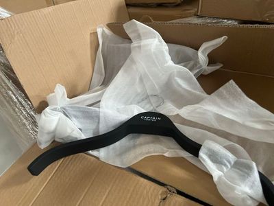 un cintre en plastique noir dans une boîte recouverte d'un tissu blanc