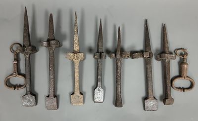 six vieux outils en fer sont alignés sur une surface blanche