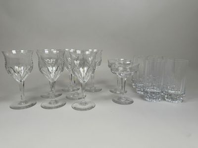 six verres à vin en cristal et un gobelet en verre posés sur un plan de travail blanc