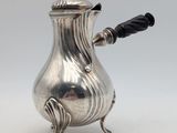 une cafetière ancienne en argent avec une poignée noire sur une surface blanche