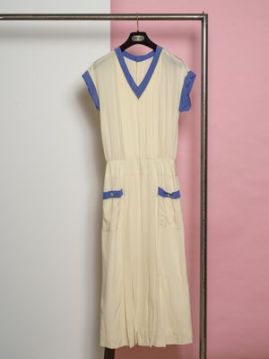 une robe beige et bleue suspendue à un cintre devant un mur rose