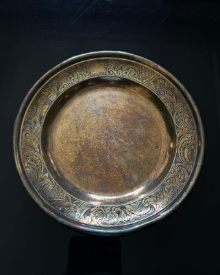 a silver plate on a stand on a black surface