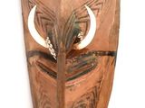 a wooden mask hanging on a wall on a white background