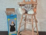 une poupée assise dans une chaise haute à côté d'une boîte