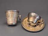 two silver cups and saucers on a saucer on a table