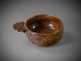 an old wooden bowl with a leaf handle on a gray surface