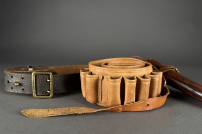two leather belts and a leather knife on a gray surface