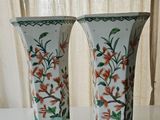 two vases sitting on a table with a curtain in the background