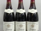 three bottles of wine sit on a wooden stand in front of a white wall