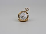 une montre de poche en or avec un cadran blanc sur une surface blanche