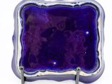 a purple glass plate with a silver rim on a white surface