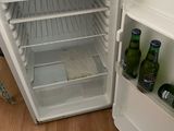 a small white refrigerator with two bottles of beer inside of it
