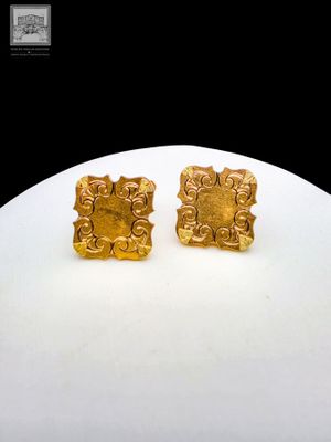 une paire de boucles d'oreilles en or posée sur une assiette blanche avec un fond noir