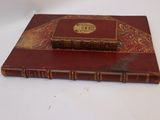 a red book with gold trim sitting on a white table