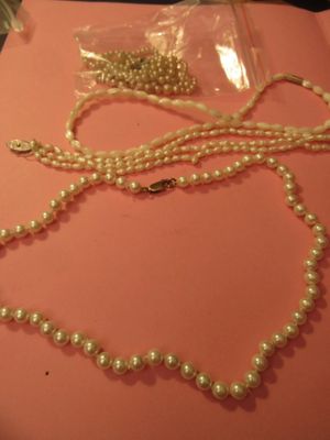 un collier de perles blanches muni d'un fermoir en or, posé sur une table rose