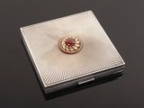 a close up of a silver box with a red stone in it