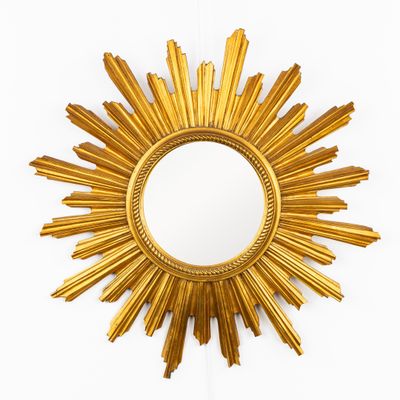 un miroir doré en forme de soleil rayonnant accroché à un mur blanc