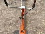 an orange string trimmer on the ground next to a pair of shoes