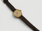 gros plan d'une montre sur une surface blanche avec un bracelet marron