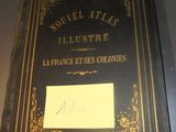 une affiche accrochée au mur d'un restaurant sur laquelle on peut lire : « Nouveau Atlas illustré de la France et de ses colonies »