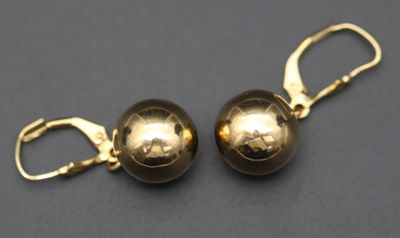 une paire de boucles d'oreilles en forme de boules dorées posées sur une surface noire