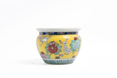 un vase jaune orné de fleurs, posé sur une surface blanche