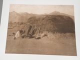 two men sitting outside of a small hut in the desert