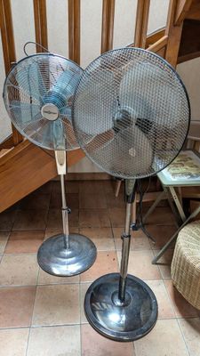 deux ventilateurs métalliques posés par terre l'un à côté de l'autre