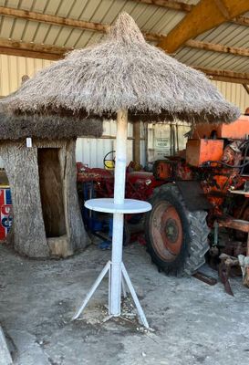 un parasol au toit de chaume au milieu d'une grange, avec un tracteur en arrière-plan