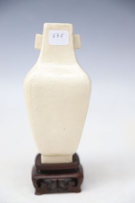 un petit vase blanc posé sur un socle en bois, lui-même posé sur une surface blanche