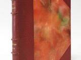 an old book with a red cover sitting on top of a white table