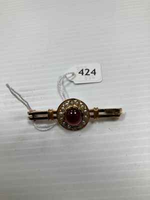 un gros plan d'une broche rouge et dorée posée sur une surface blanche