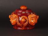 an orange and brown ceramic jar with three faces on it