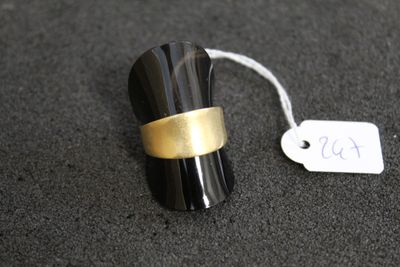 une bague noire et dorée posée sur une surface noire, avec une étiquette de prix