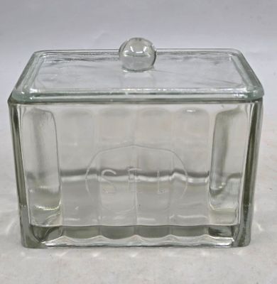une boîte en verre avec un couvercle en verre, posée sur une surface blanche