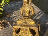 brass statue of a buddha sitting on a bench in a garden