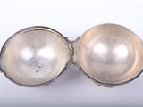 an old silver egg with a pearl inside on a white surface