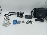 a camera, a camera case, a flash drive, and other electronics laid out on a white surface