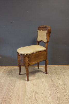 une vieille chaise en bois avec un coussin posé dessus, devant un mur gris