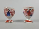 pair of porcelain cups with painted figures on them sitting next to each other