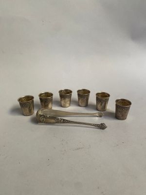 six verres à shot en argent et une cuillère posés sur un plan de travail blanc