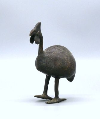 a small bronze statue of a bird on a white surface