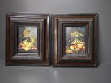 une paire de tableaux encadrés représentant des fruits et des fleurs posés sur une table