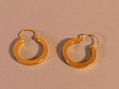 une paire de boucles d'oreilles créoles dorées sur fond beige
