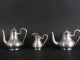 three silver teapots on a black background