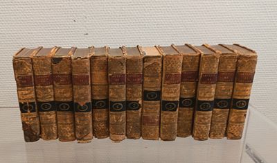 Plusieurs livres anciens sont empilés les uns sur les autres dans une vitrine.
