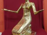 statue d'une femme vêtue d'une robe dorée, assise sur un socle rouge