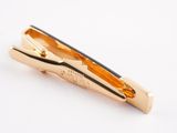 a close up of a gold tie clip on a white surface