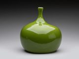 un vase vert posé sur une surface blanche, avec un fond gris